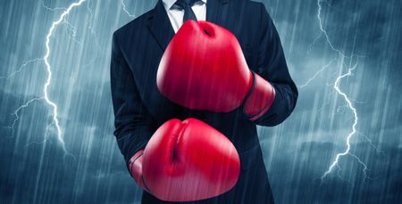 A dangerous sales person getting ready for a fight concept with red boxing gloves and thunder lightning in background.