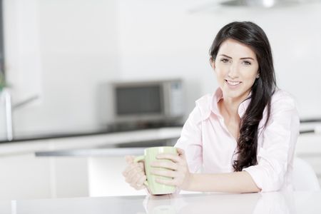 Young woman in pink shirt sitting at dining table at home drinking a hot drink.