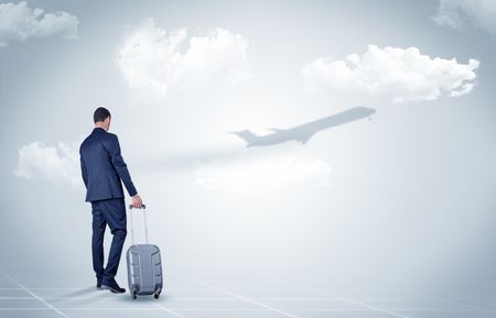 Young businessman with luggage walking towards an looking to a raising airplane