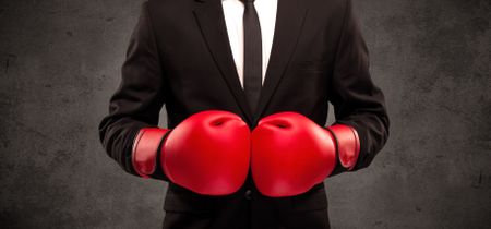 A well dressed sales person standing with red boxing gloves on his hand in front of urban grey wall background concept.