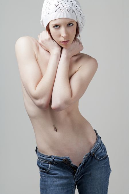Young woman posing in open jeans and covering her chest with her hands, whilst wearing a white beanie hat