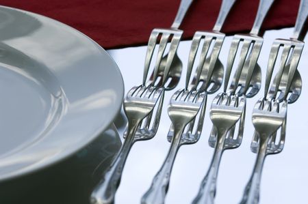 Four forks and their reflections against light blue sky beside a dinner plate