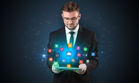 Handsome businessman in suit with tablet on his hand and application icons above