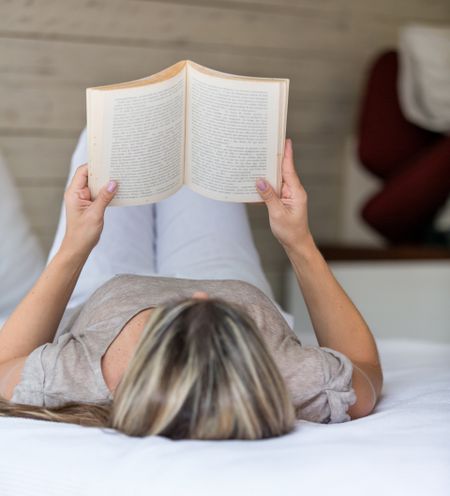 Relaxed woman lying in bed reading a book