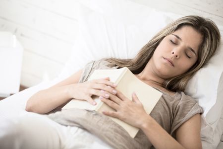 Woman falling asleep while reading a book in bed