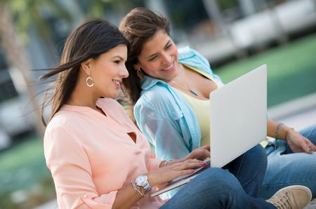 Female friends using a laptop at the park and smiling