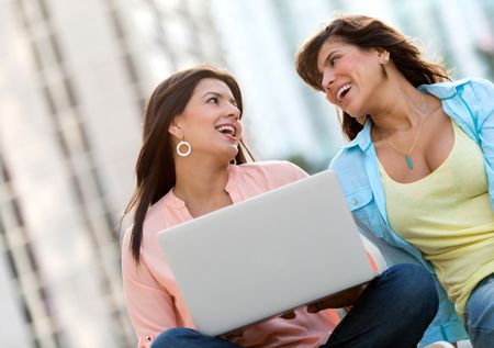 Happy women using a laptop outdoors for social networking