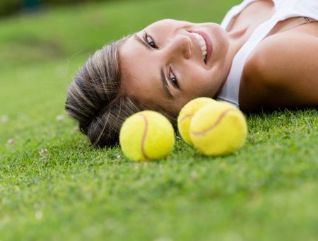 Female tennis player lying on the lawn with balls