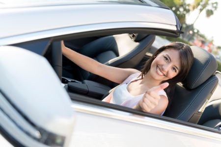 Happy woman smiling in a car with thumbs up