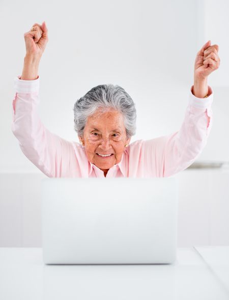 Happy elder woman with a laptop and arms up