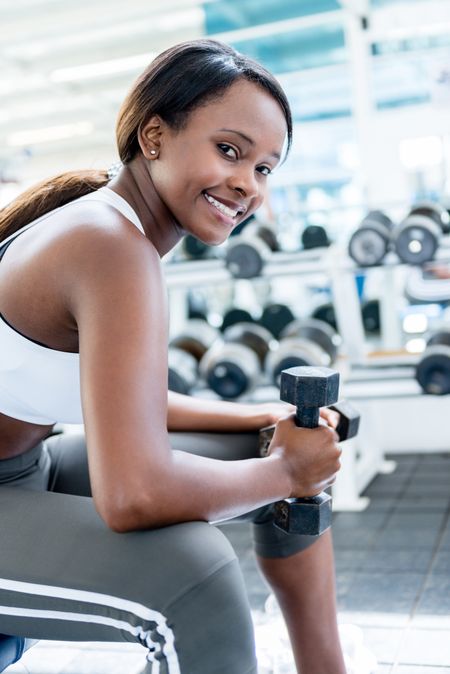 Gym woman exercising with free weights and smiling