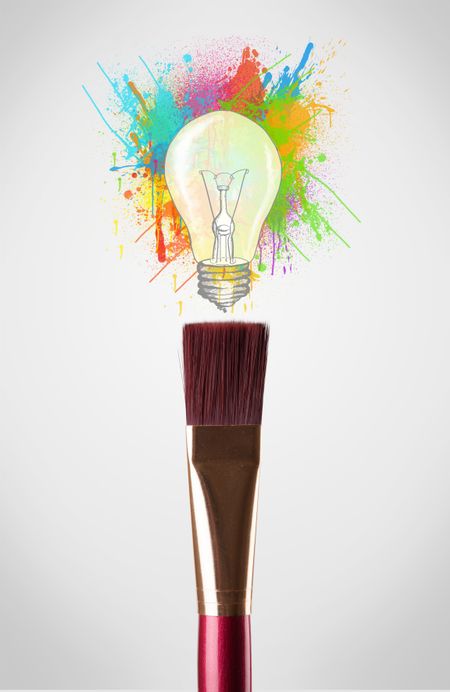 Paintbrush close-up with colored paint splashes and lightbulb concept