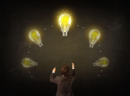 Young businessman thinking in front of a blackboard with glowing lightbulbs over his head