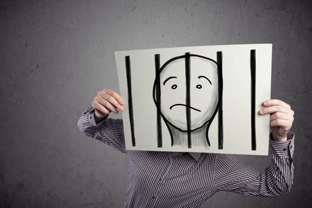 Businessman holding a paper with a prisoner in jail behind the bars on it in front of his head
