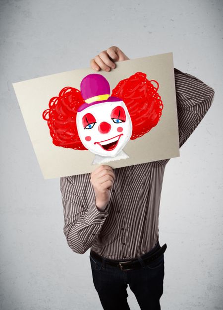 Young businessman holding a cardboard with a clown on it in front of his head