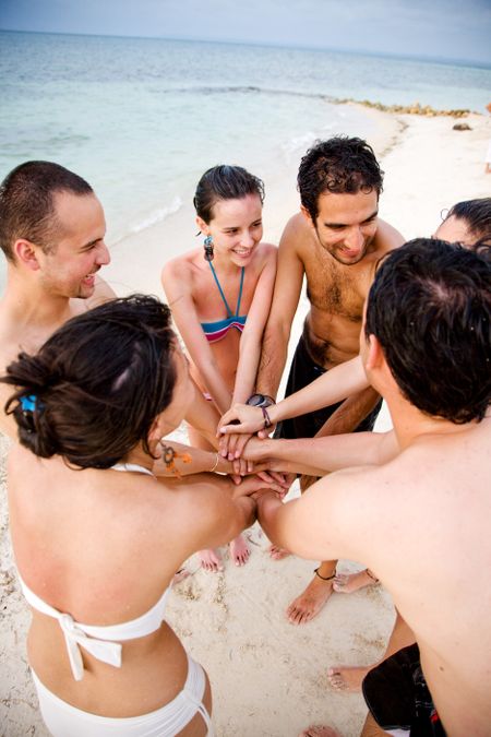 happy group of friends smiling outdoors at the beach with their hands together