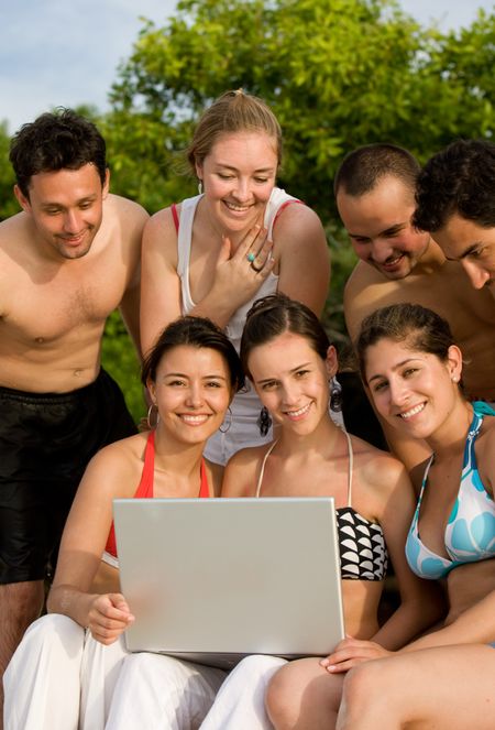 Happy group of friends smiling at the beach with a laptop computer
