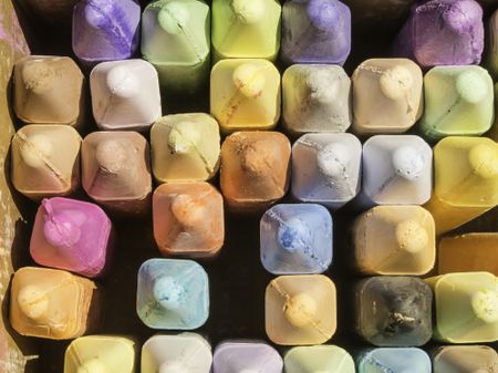 Overhead view of pastel-colored chalk sticks in open box used by sidewalk artist on a sunny afternoon