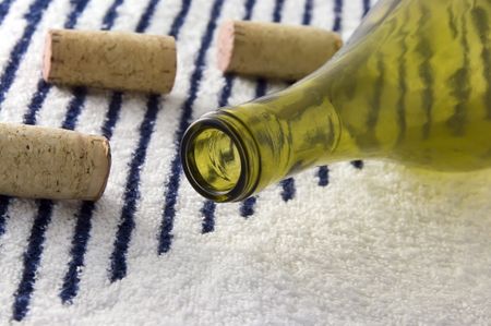 Green wine bottle and three corks on striped white beach towel