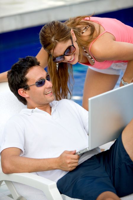 couple using a laptop while relaxing by the swimming pool