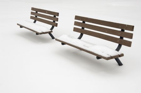Two snow-covered benches by a tennis court under snow