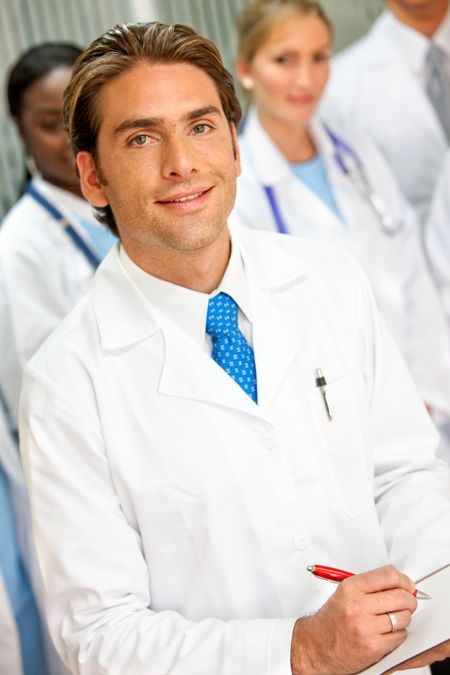 male doctor smiling with his team behind in a hospital