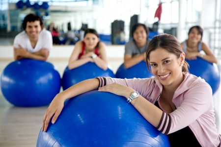 Woman portrait at the gym leaning on a pilates ball in front of a group