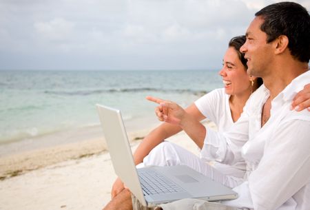 Beach couple on a laptop during vacations