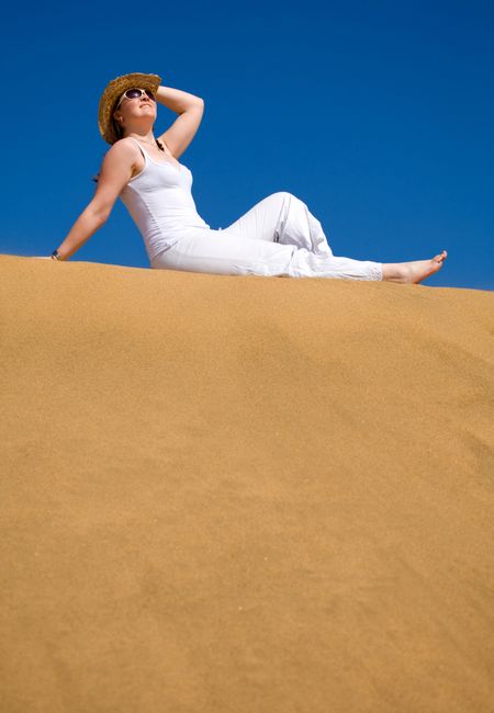 Beautiful girl lying by the beach on a sand dune wearing a hat and sunglasses