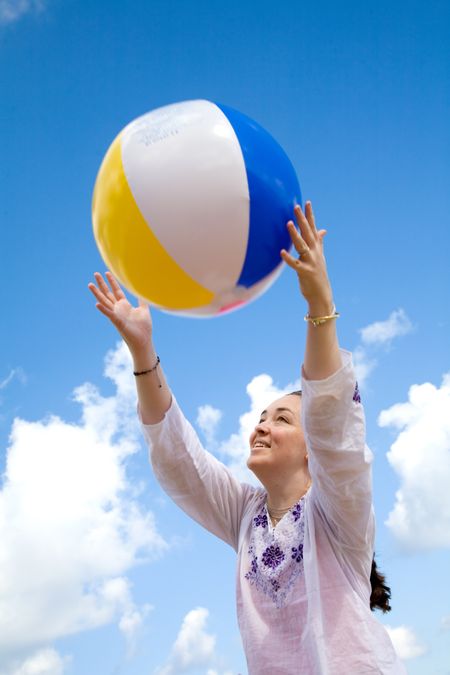 beautiful girl playing with a beachball at the beach in front of a beautiful blue sky
