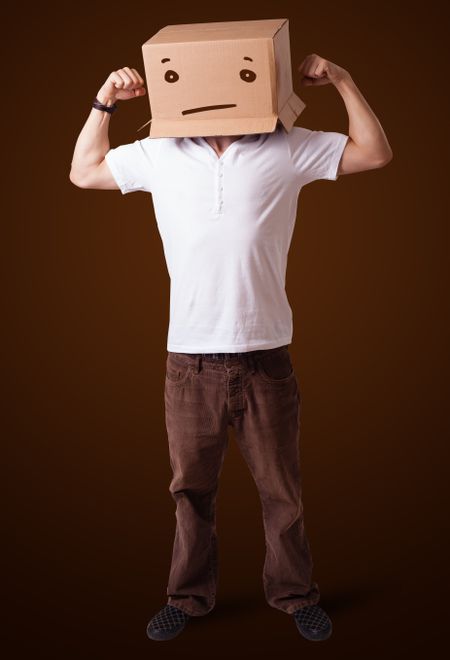 Young man standing and gesturing with a cardboard box on his head with straight face