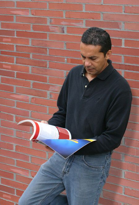 casual guy reading a magazine against a red brick wall