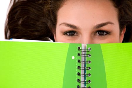 beautiful female student peeping over a green notebook while lying on the floor on a white background