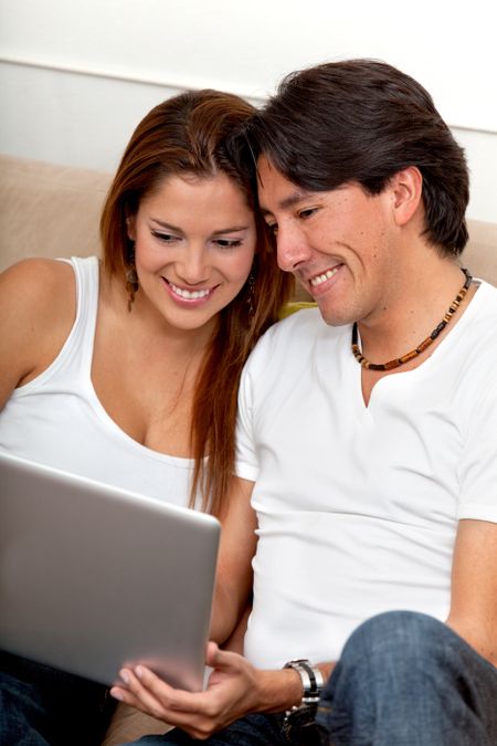 Couple's portrait sitting on the sofa with a laptop computer