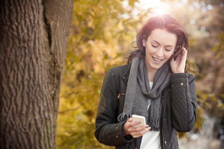 Young woman enjoying a autumn walk while texting with friends on her phone