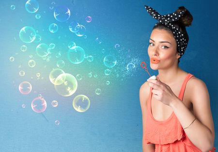 Pretty lady blowing big colorful bubbles on blue background