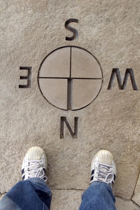 Two feet standing by directional map in stone, east west north south