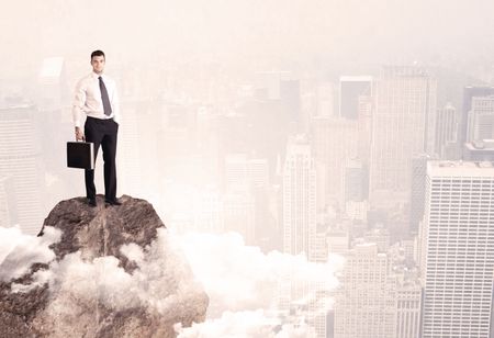 An elegant professional business male standing on top of a high cliff above the clouds looking at the city concept