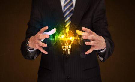 Businessman holding a shining light bulb in front of his body
