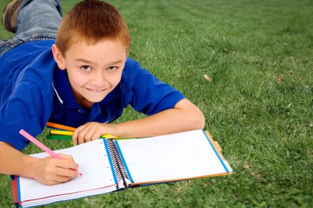 Boy lying on the grass coloring a notebook