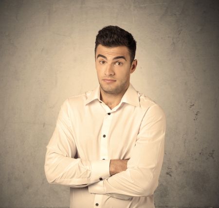 A young handsome business person making facial expression in front of clear, empty concrete wall background concept