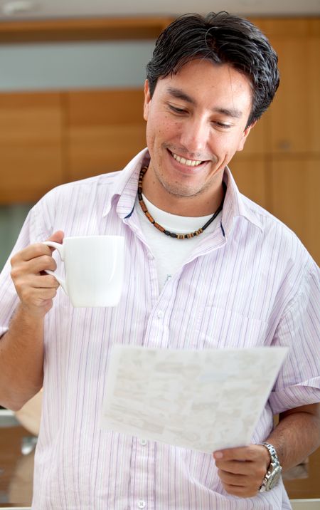 Smiley man indoors reading a paper and drinking coffee