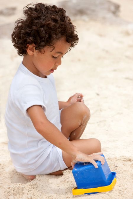 Young boy making a castle with sand and a bucket