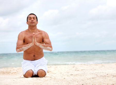 Handsome man practicing yoga exercises at the beach