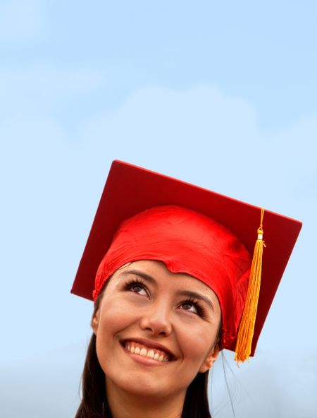 Pensive graduation woman in red mortarboard outdoors