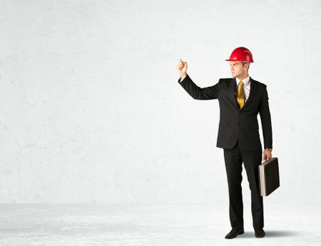 A young architect in red safety helmet planning and drawing with a pen in his hand in empty space in front of a white background.