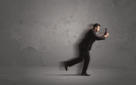 Running businessman in a rush with device in hand on background