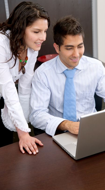 business couple browsing on a laptop - smiling in an office