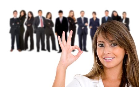 Businesswoman doing the ok sign with her team behind isolated on white