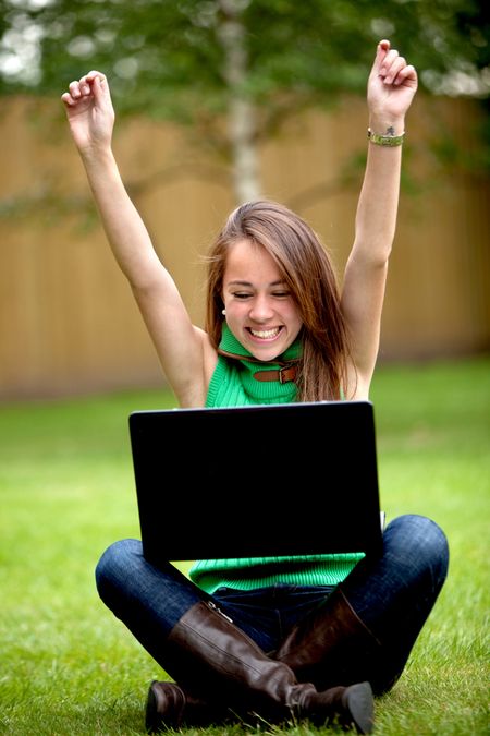 casual success girl on a laptop with arms up outdoors